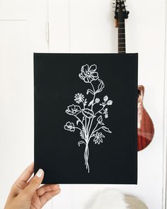 a person holding up a black paper with white flowers on it in front of a guitar