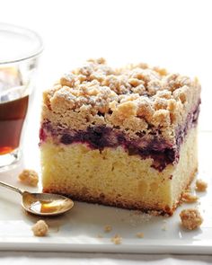 a piece of cake on a plate next to a cup of tea and spoons