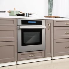 an oven in the middle of a kitchen with gray cabinets and white counter tops on both sides