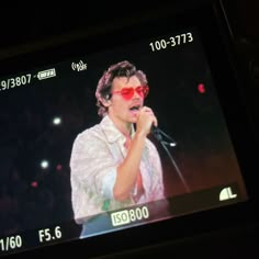 a man with sunglasses on singing into a microphone in front of a screen showing the time