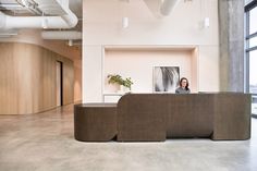 a woman is sitting at the front desk in an office with large windows and concrete flooring