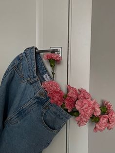 a pair of jeans hanging on a door with pink flowers in the pocket and behind it is a blue jean jacket