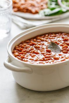 a white pot filled with baked beans on top of a table next to a plate