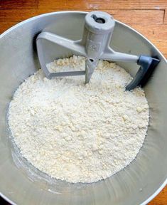 a metal bowl filled with flour on top of a wooden table