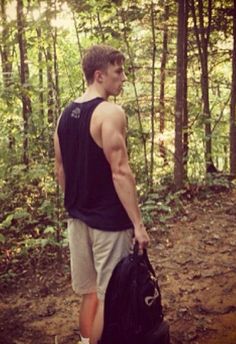 a young man carrying a black bag in the woods