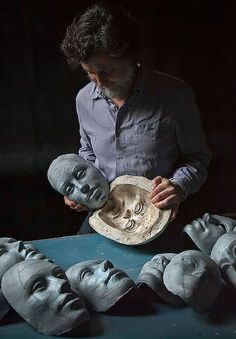 a man is working on clay sculptures with his head in the shape of people's heads