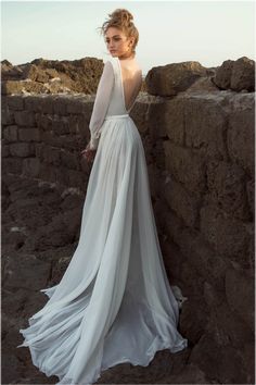 a woman in a white dress leaning against a stone wall with her back to the camera