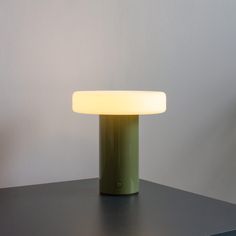 a green table lamp sitting on top of a black table next to a white wall