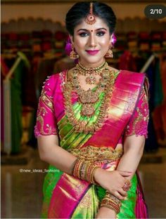 a woman in a pink and green sari with gold jewelry on her neck, standing next