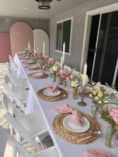 the table is set with pink and white flowers in vases, plates and napkins