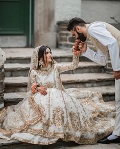 a man kneeling down next to a woman in a wedding dress on the steps outside