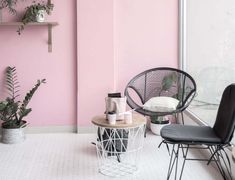 two chairs and a table in a room with pink walls, plants and other items