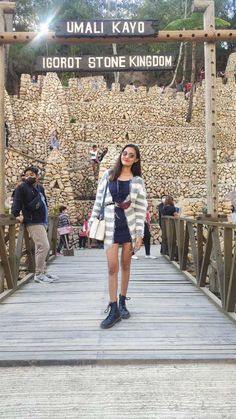 a woman standing on a wooden bridge in front of a sign that says umali kavo