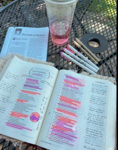 an open book sitting on top of a table next to a cup and pencils