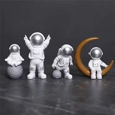 three small astronaut figurines standing next to each other with the moon in the background