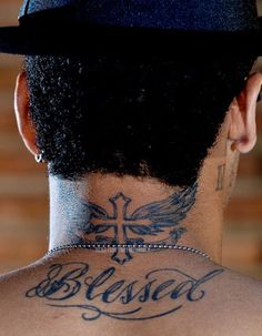 the back of a man's head with tattoos on his neck and cross behind him