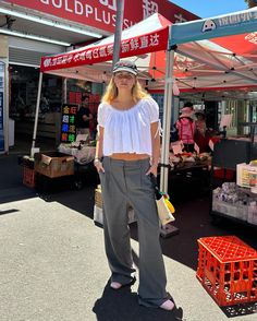 a woman standing under a red and white sign in front of a food stand on the street