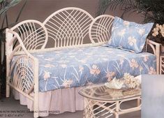 a white wicker day bed sitting next to a glass table with flowers on it