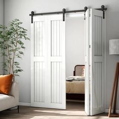 an open white barn door in a living room next to a couch and potted plant