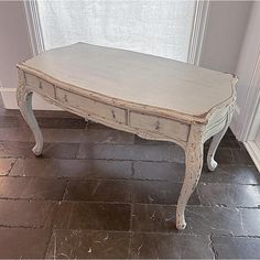 an old white table sitting on top of a tile floor next to a window in a room