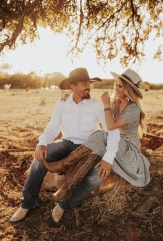 a man and woman sitting under a tree in the middle of an open field together