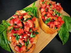 two pieces of bread with tomatoes and basil on them sitting on a wooden cutting board