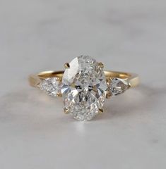 an oval cut diamond with three pear shaped diamonds on the side, set in yellow gold