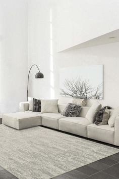 a living room with white walls and black flooring is pictured in this image, there is a large sectional couch on the far side