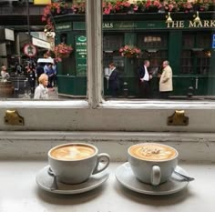 two cups of cappuccino sit on a window sill in front of people