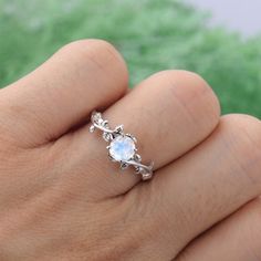 a woman's hand holding a ring with an opal in the middle and leaves around it