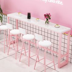 three pink and white stools sitting next to a counter with flowers on it in front of a pink wall