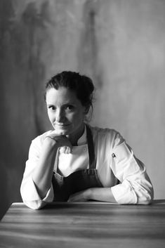 a black and white photo of a woman sitting at a table with her hands on her chin