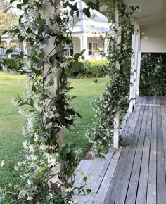 a wooden porch covered in vines and flowers next to a white house with large windows