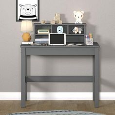 a desk with a laptop, lamp and teddy bear on it in front of a gray wall