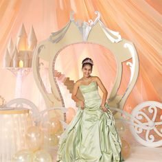 a woman in a green dress standing next to a princess carriage and table with balloons