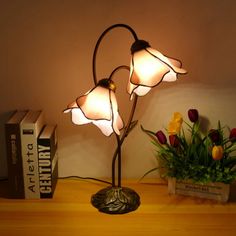 a lamp that is sitting on top of a table next to some books and flowers