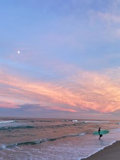 a person with a surfboard standing in the water at sunset or sunrise on an ocean beach