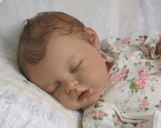 a baby doll is sleeping on a white blanket with pink flowers around it's head