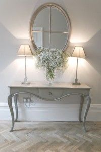 a vase with flowers on top of a table in front of a mirror and lamp