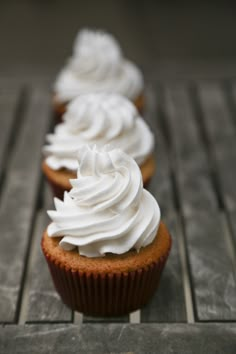 three cupcakes with white frosting are lined up