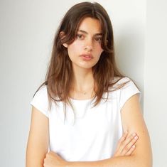 a woman standing with her arms crossed and looking at the camera while wearing a white t - shirt