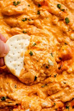 a cracker being dipped into a cheesy dip