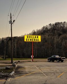 a yellow dollar general sign sitting in the middle of a parking lot next to a black truck