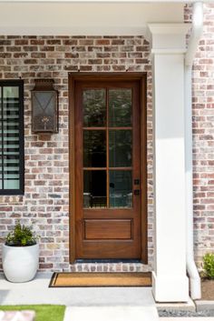 a white planter sitting in front of a wooden door on a brick building with black shutters