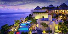 an outdoor swimming pool next to the ocean at dusk with lit up buildings in the background