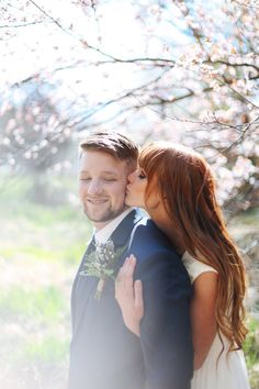 a bride and groom kissing in front of blossoming trees