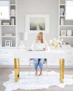 a woman sitting at a white desk with a laptop on her lap and gold legs