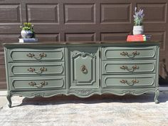 an old dresser painted in green with gold handles and knobs on the top, sitting next to a garage door