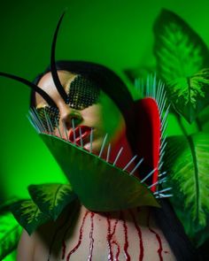 a woman with long black hair and green leaves on her head is surrounded by plants