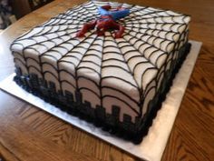 a spider - man cake on a wooden table with white frosting and black icing